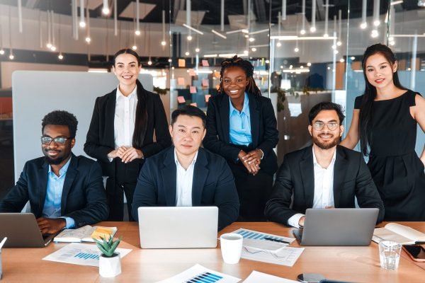 Team of successful young business workers in formal suits with laptops in modern office. Young people of different nationalities working in a coworking space.