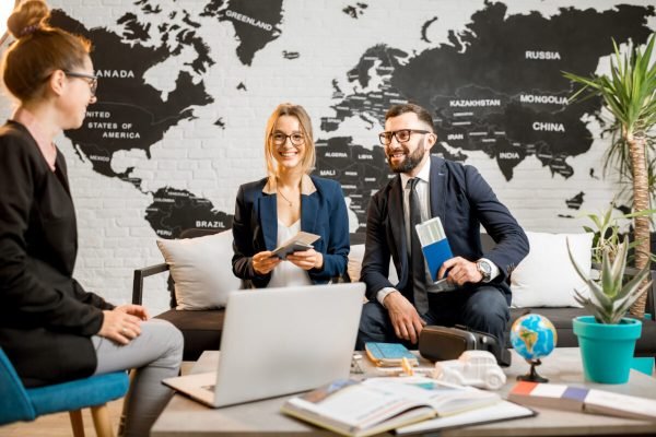 Young businesscouple choosing a trip with agent sitting at the travel agency office with world map on the background